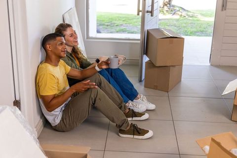 Young multiethnic couple taking coffee break while unpacking boxes in new home entryway
