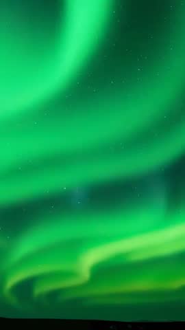 Vertical aurora borealis video showing green curtains swirling over dark horizon