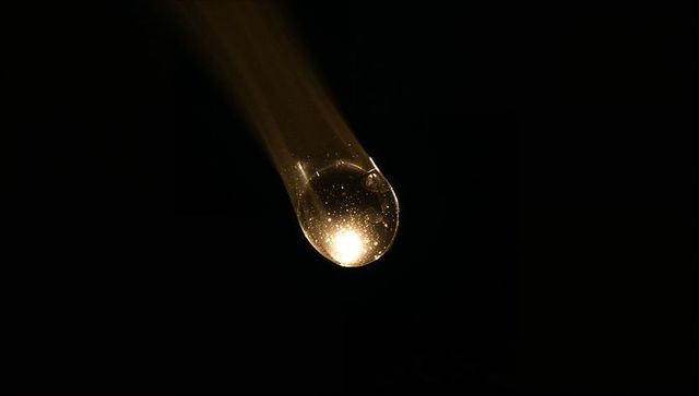 Golden droplet clinging to glass pipette, macro glow with bubbles and motion trail