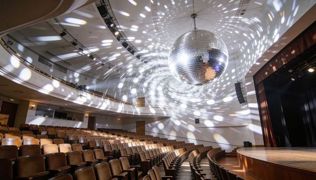 Casting mirrored disco ball projecting swirling reflections across theatre auditorium