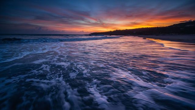 Sunset reflections on wet sand with rolling surf and twilight sky, headland silhouette