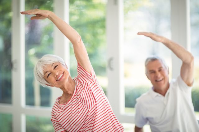 Senior couple engaging in stretching exercises at home, promoting a healthy and active lifestyle. Ideal for use in health and wellness articles, fitness programs for seniors, retirement living promotions, and advertisements focusing on active aging.