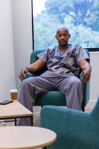 African american clinician relaxing in clinic lounge wearing gray scrubs and id lanyard