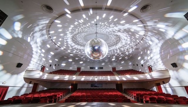 Mirrored disco ball scattering sparkling light across vintage theater auditorium with balcony