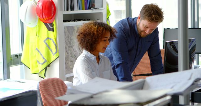 Two architects are seen collaborationg over a design project in a modern office setting. They are focused on plans and documents, conveying a professional and dedicated atmosphere. This image is perfect for content related to workplace collaboration, architecture, construction industry, team projects, gender diversity in the workforce, or modern work environments.