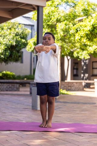 African american boy practicing yoga outdoors on purple mat in sunlit brick courtyard