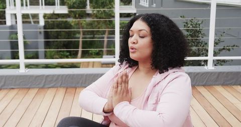 Plus-size woman practicing rooftop meditation and deep breathing in pink activewear