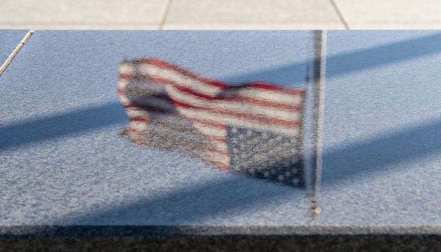 Granite reflecting american flag and flagpole with long shadows on memorial plaza surface