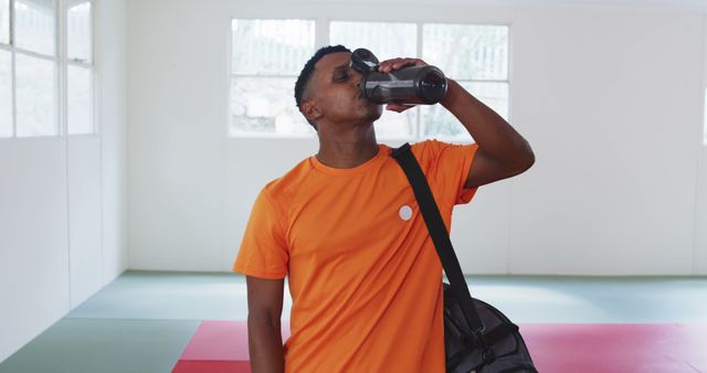 Man standing in gym with a gym bag, hydrating after workout. Suitable for promotions related to fitness and sports, gym advertisements, hydration importance campaigns, and gym gear. Highlighting healthy lifestyle, exercise routines, and sports equipment.