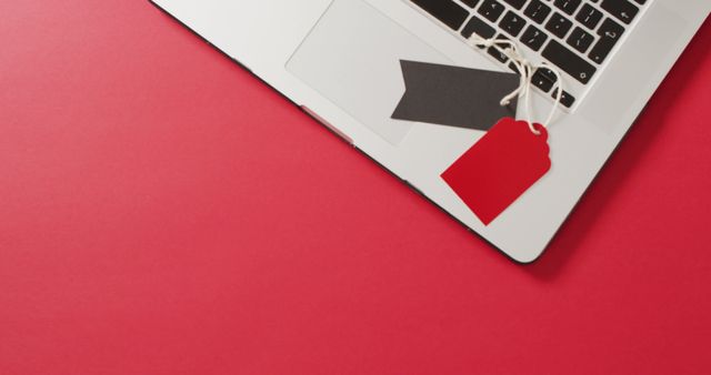 Overhead view of laptop with black and red sale tags on red background. Luxury treat, present, online shopping, black friday, sale and retail concept digitally generated image.