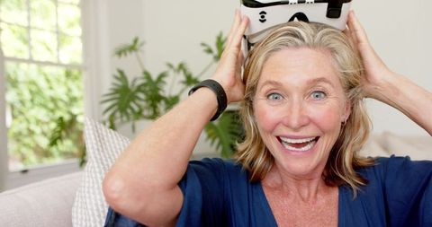 Excited mature woman using virtual reality headset at home