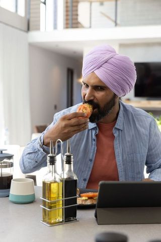 Indian Man in Lilac Turban Eating Sandwich in Modern Kitchen