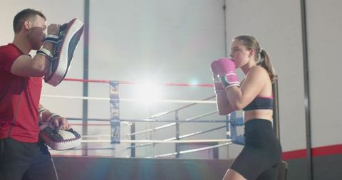Female boxer training with coach holding focus mitts in boxing ring with pink gloves