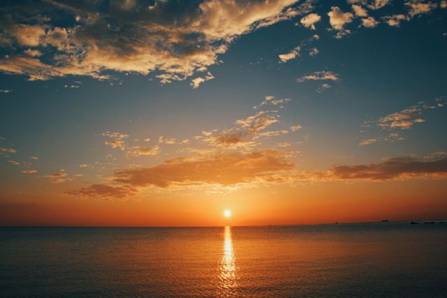 This image captures a breathtaking sunset over the ocean, with a vibrant orange sky and a smooth, reflective water surface that creates a serene and peaceful atmosphere. An excellent choice for promoting travel and tourism, decorating living spaces, and creating a calming ambiance. Perfect for advertisements, websites, and social media that focus on nature, relaxation, and coastal living.