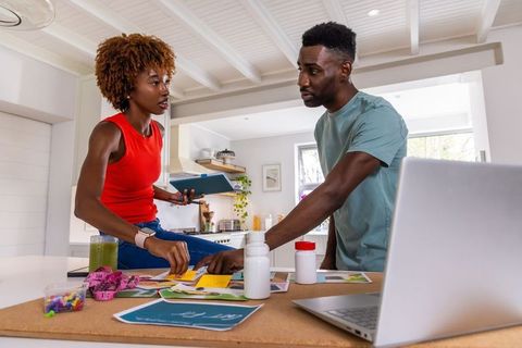 African american couple planning kitchen renovation on bright island with laptop, color swatches and
