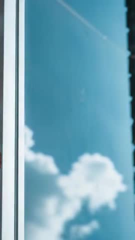Recording sky moving past window glass, showing drifting clouds, contrail, urban edge