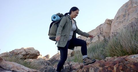 This image depicts a woman actively hiking in rocky mountain terrain, carrying a backpack with a yoga mat. Ideal for illustrating adventures in nature, outdoor fitness activities, or inspiring travel content. Useful for promoting hiking gear, outdoor destinations, or wellness in natural settings.