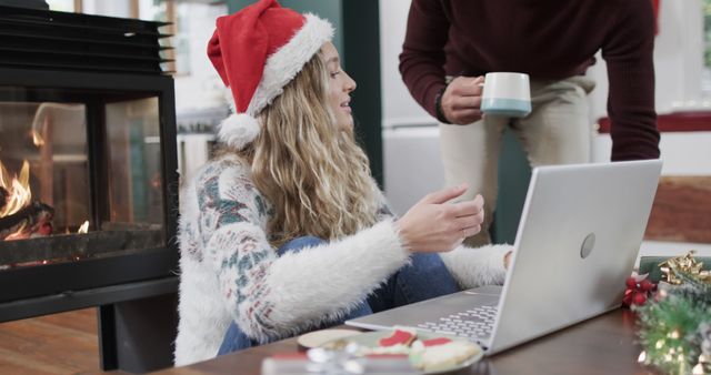 Woman in festive sweater using laptop near fireplace at Christmas - Download Free Stock Images Pikwizard.com