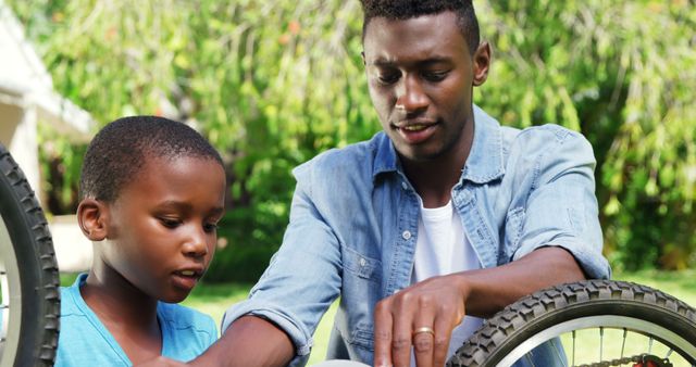 Father showing his son how to repair a bicycle outdoors provides strong themes of family bonding, fatherhood, and teaching. Suitable for use in advertisements, educational materials, and articles focusing on parenting, outdoor activities, and life skills.