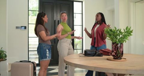 Friends greeting and discussing travel plans in modern sunlit foyer with luggage