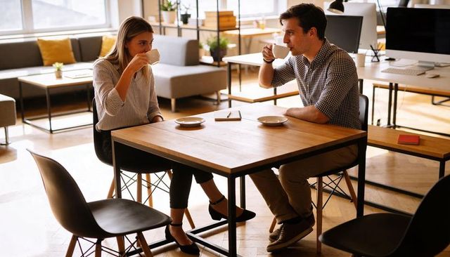 Coworkers having coffee and chatting at wooden table in bright modern coworking lounge