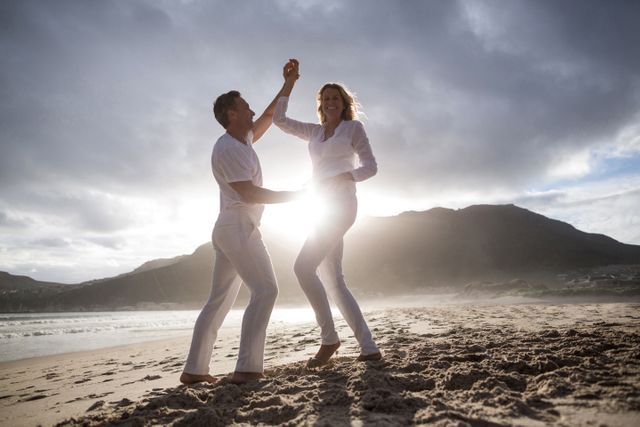 Couple enjoying a playful moment while dancing on a beach at sunset. Ideal for content on love, relationships, lifestyles, and travel. Could be used in advertisements, blog posts, or brochures promoting romantic getaways, leisure activities, or senior lifestyle products.