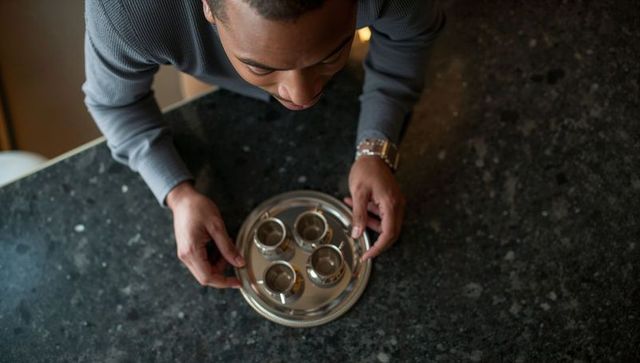 Man leaning over kitchen counter holding silver tray with four cups