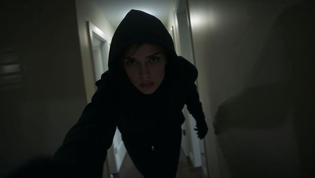 Hooded woman reaching toward camera in narrow home hallway backlit dramatic closeup