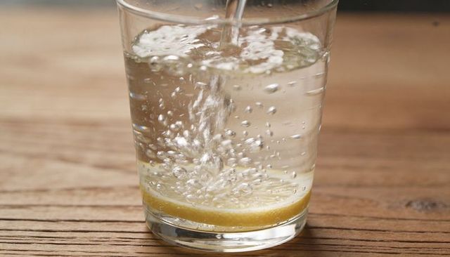 Pouring sparkling water over lemon slice in glass on wooden table with visible bubbles