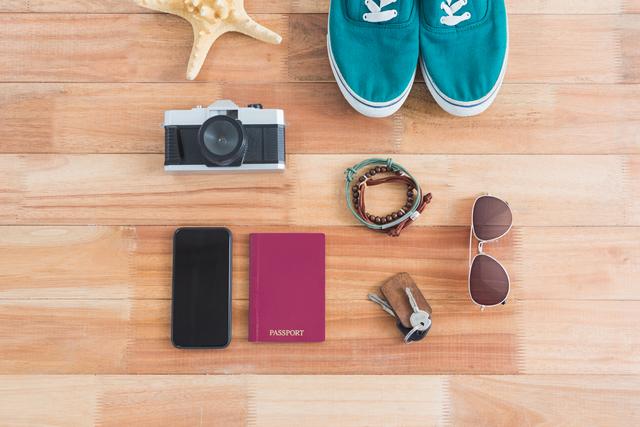 Flat lay of travel essentials including passport, camera, smartphone, sunglasses, shoes, and accessories on wooden surface. Ideal for travel blogs, vacation planning, packing tips, and adventure-themed content.