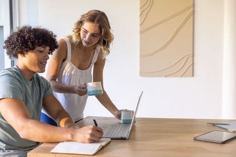Couple collaborating in sunlit modern home workspace with laptop and coffee