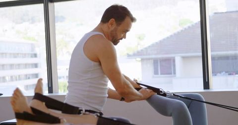 Male Pilates Instructor Adjusting Reformer Straps During Therapeutic Workout Session