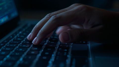 Typing on backlit laptop keyboard at night with blue glow for cybersecurity, coding