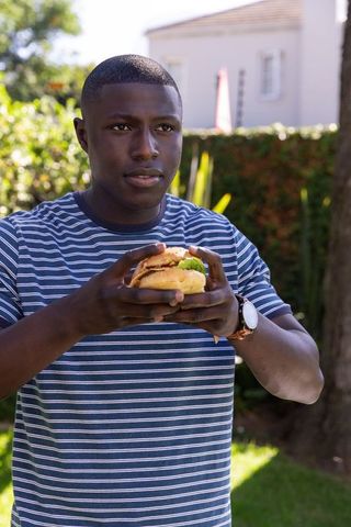 Man Enjoying Hamburger While Checking Time Outdoors