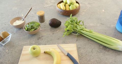 Healthy smoothie prep on marble countertop with cutting board, banana, apple, celery