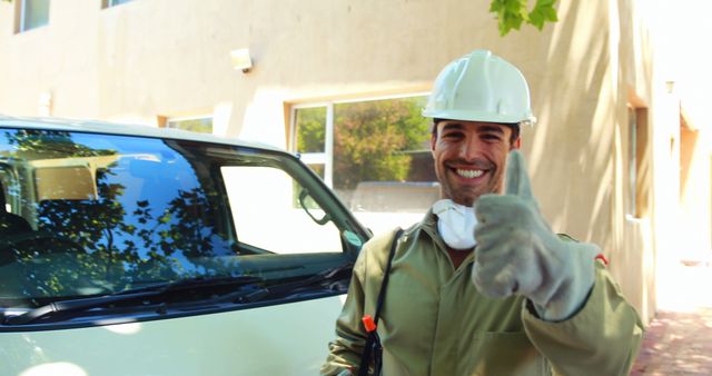 Smiling construction worker wearing protective gear is giving thumbs up while standing beside a vehicle outdoors. Great for content related to safety at work, positivity in the workplace, or construction industry marketing materials.