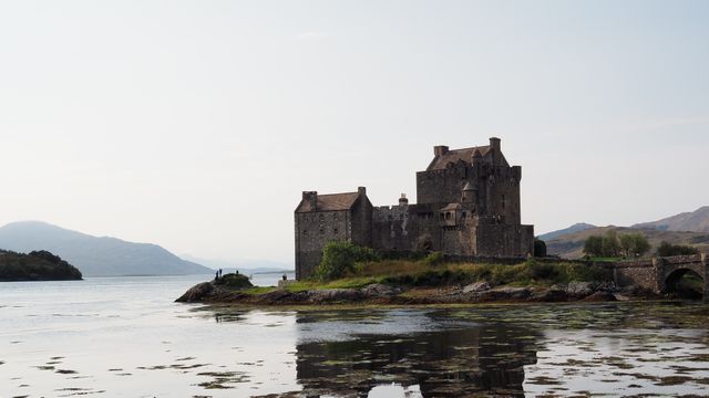 Picture shows a historic Scottish castle situated on the edge of a calm lake, with mountainous backdrop and clear sky. Ideal for promoting travel destinations, medieval history, and natural beauty. Suitable for travel blogs, tourism websites, and historical documentaries.