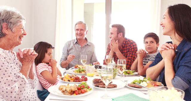Multigenerational family gathered at home, enjoying a meal and expressing gratitude through prayer. Perfect for illustrating family values, celebration of togetherness, and shared moments. Ideal for use in lifestyle blogs, family-oriented advertisements, and holiday-related content.