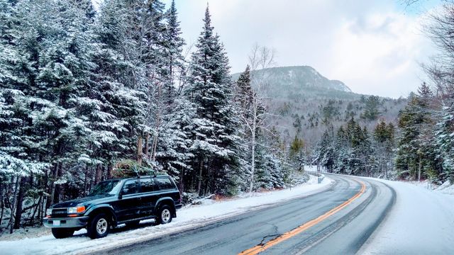 Snow-covered trees flank a winding mountain road with an SUV parked along the side. Ideal for illustrating winter travel, scenic drives, outdoor adventures, Christmas, holiday journeys or wintery landscapes for travel promotions, holiday cards, and marketing materials emphasizing scenic winter road trips.