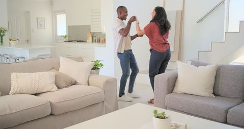 Modern couple dancing in bright minimalist living room holding hands, open-plan lifestyle