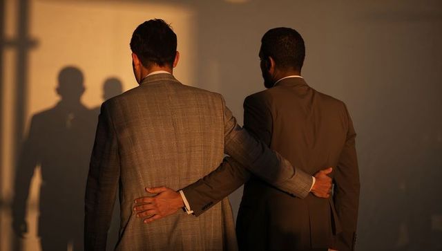 Business partners walking linking arms in backlit office corridor showing professional unity