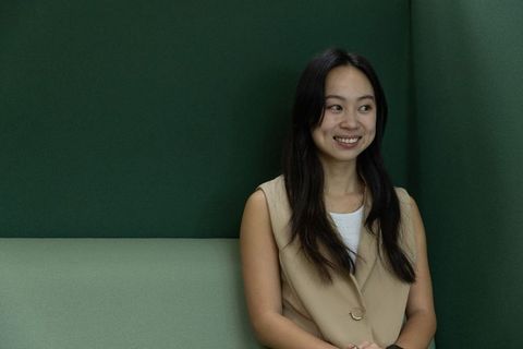Asian woman smiling while sitting in modern green office alcove wearing beige blazer