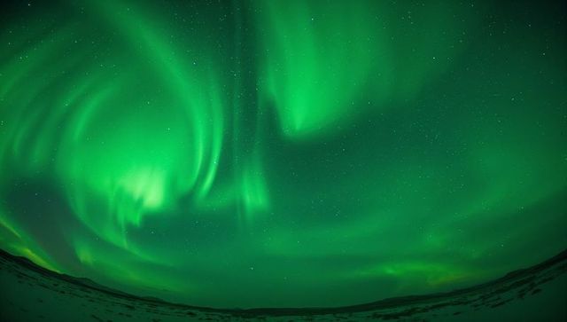 Emerald aurora swirling over snowy Arctic tundra under starry night sky