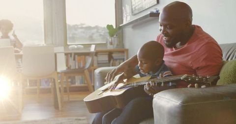 Father and Son Playing Acoustic Guitar on Living Room Sofa