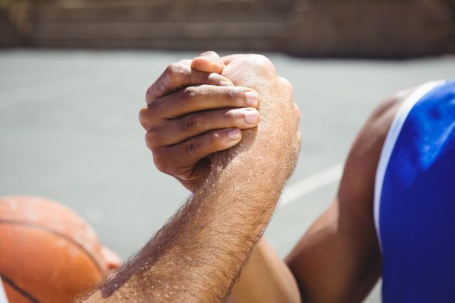 Basketball players holding hands in a gesture of unity and teamwork on an outdoor court. This image can be used to represent sportsmanship, cooperation, and the importance of teamwork in sports. Ideal for articles, advertisements, and campaigns promoting team spirit, athletic events, and community sports programs.