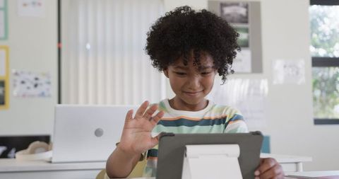 Curly-haired student raising hand using tablet for online learning in classroom