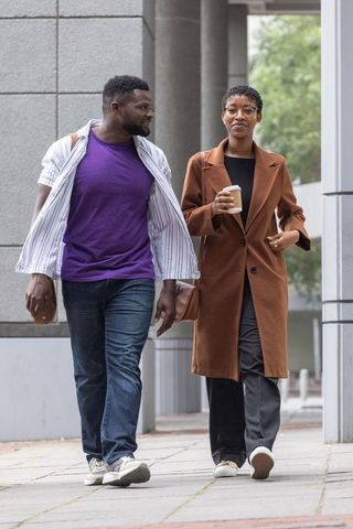 African american couple walking in city holding coffee and bag, urban casual lifestyle