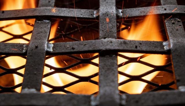 Glowing metal grill grate revealing flames through mesh with sparks and embers closeup