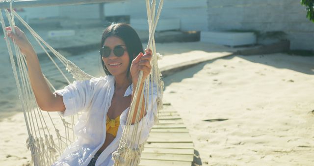 Portrait of happy hispanic woman in sunglasses sitting in hammock on sunny beach, slow motion - Download Free Stock Photos Pikwizard.com