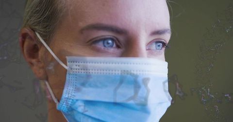 Mid-adult woman wearing blue surgical mask and gazing with bright eyes clinical closeup